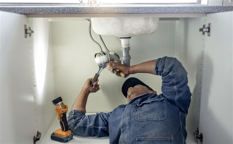 Plumber repairing pipes beneath a bathroom sink in Casa Grande