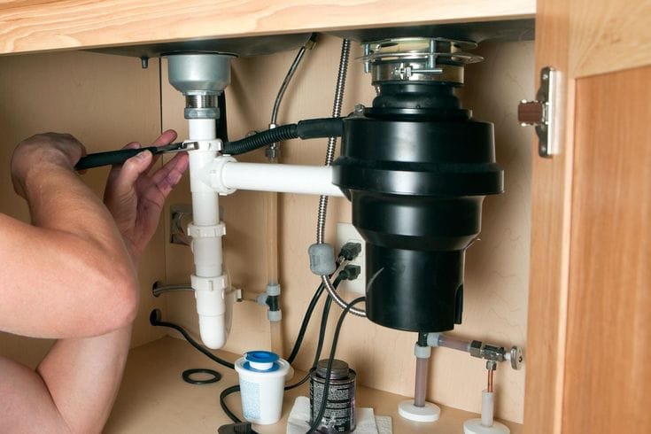Plumber installing a garbage disposal beneath a kitchen sink in Casa Grande