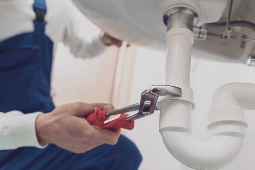 Plumber repairing a white drain pipe beneath a sink in Casa Grande