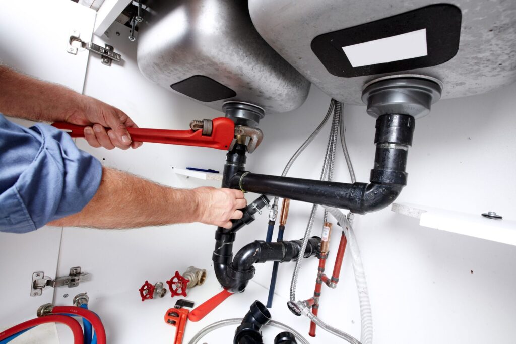 Plumber repairing drain pipes beneath a kitchen sink in Casa Grande